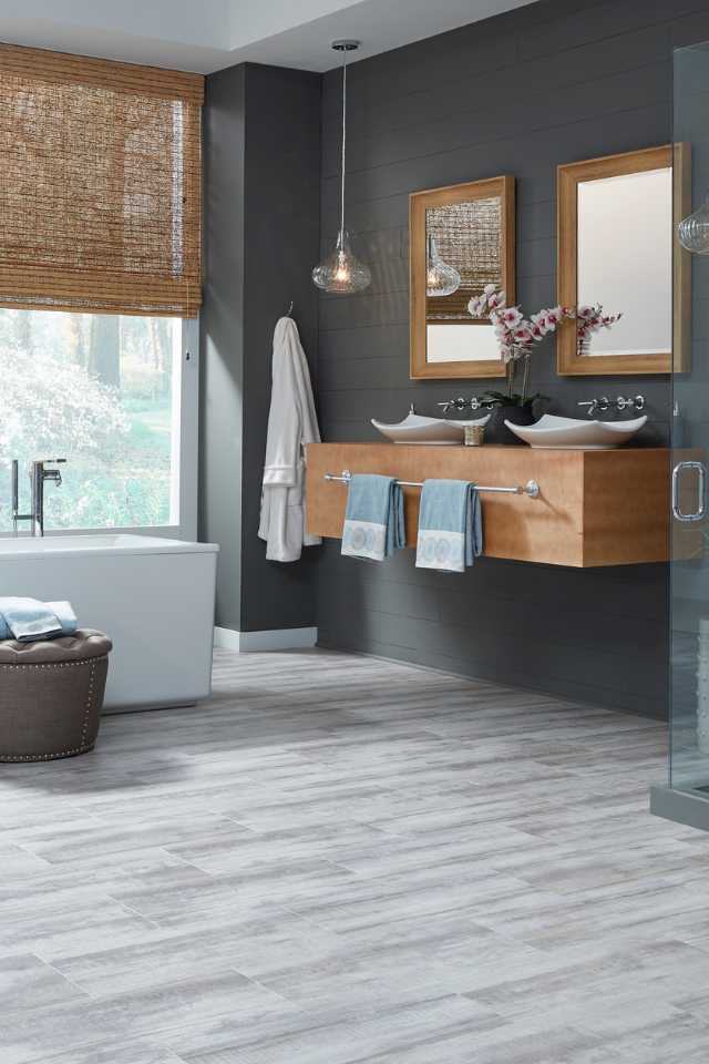 gray stone look luxury vinyl in modern bathroom with deep soak tub, gray walls and roman shades